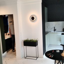 Dar-bud usługi ogólno budowlane - Nowoczesne wnętrze po remoncie: białe ściany, marmurowe płytki podłogowe, czarne akcenty, oświetlenie punktowe i dekoracje roślinne. Widok na odnowioną kuchnię.