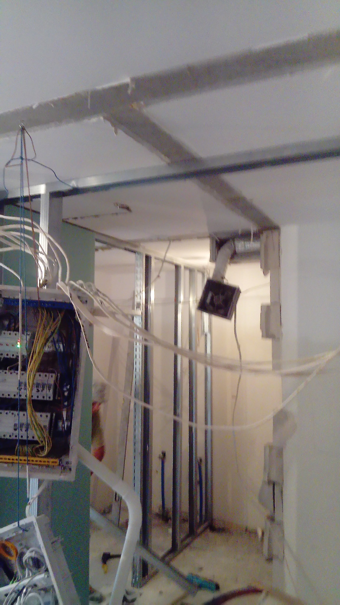 Instalacja elektryczna w trakcie montażu, widoczne przewody, puszki i metalowa konstrukcja ścianki działowej. Prace wykończeniowe w surowym wnętrzu.