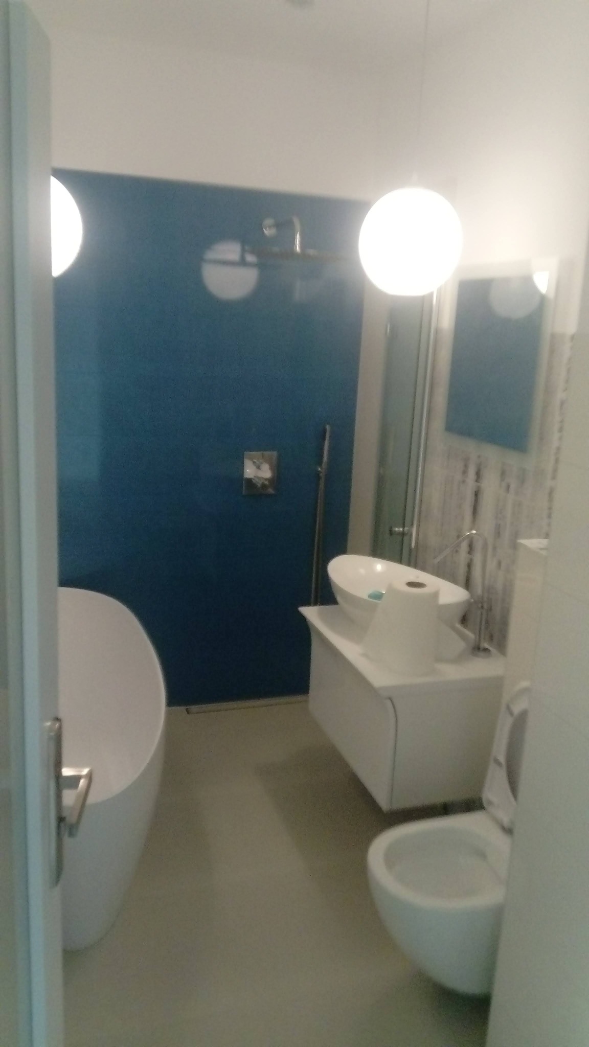 Nowoczesna łazienka w Leśniewie z wolnostojącą wanną, umywalką na szafce i toaletą. Ściana w odcieniach błękitu, minimalistyczne oświetlenie.