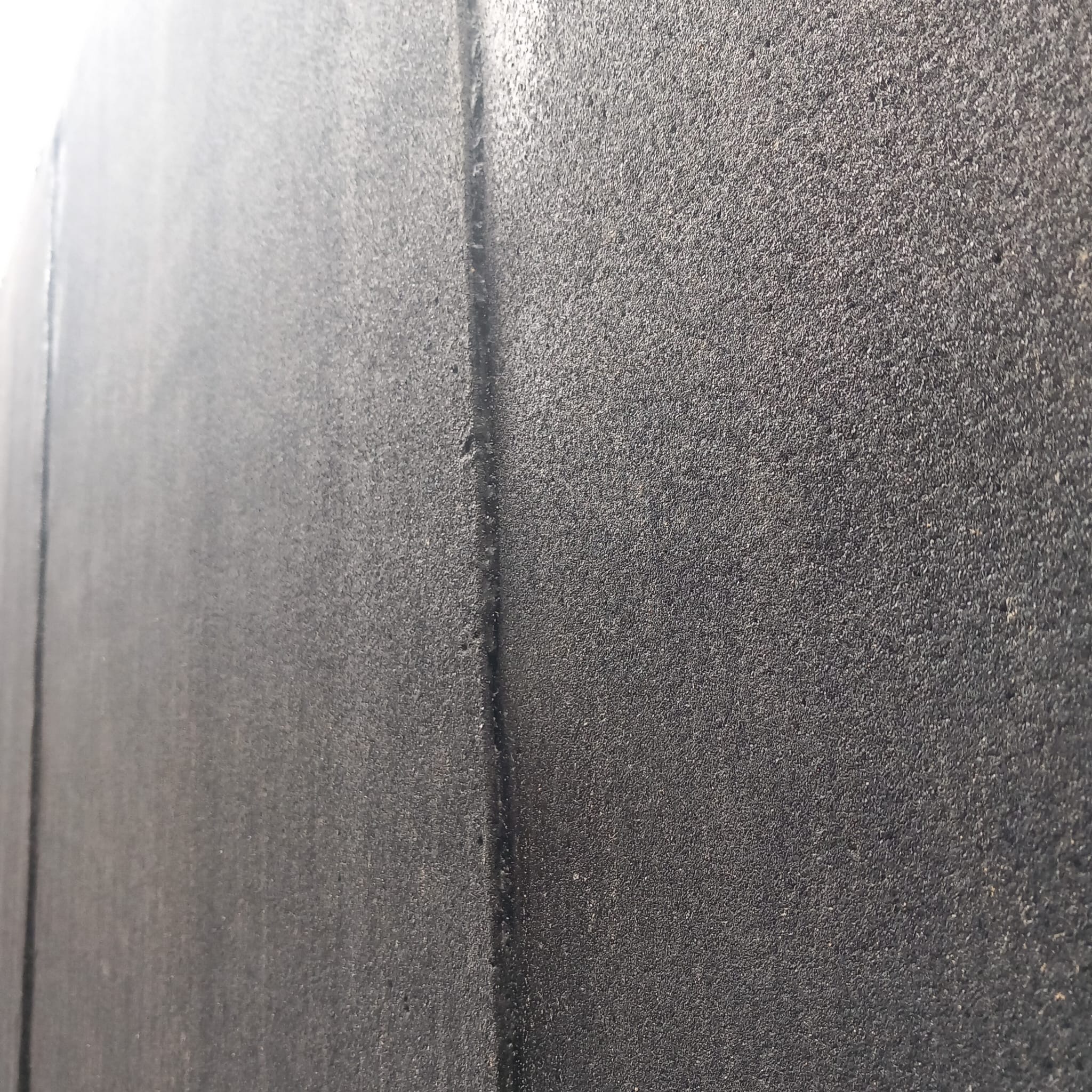 Szara, chropowata powierzchnia z pionową linią podziału, przypominająca świeżo nałożoną strukturę elewacyjną lub posadzkę żywiczną. Widoczne niedoskonałości i nierówności.