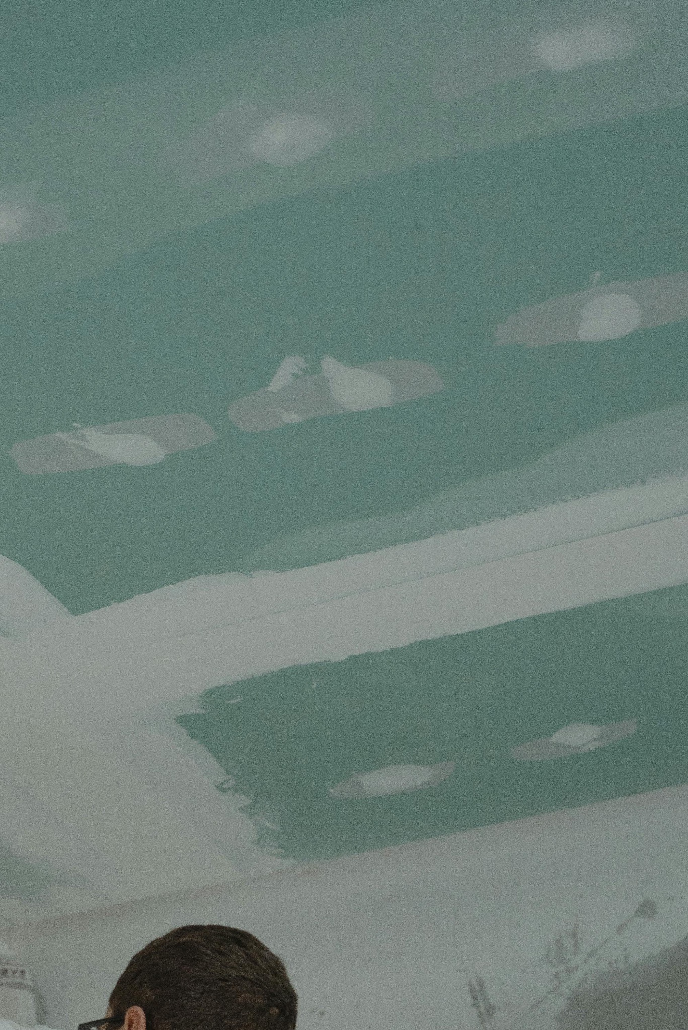 Zielony sufit z płyt kartonowo-gipsowych, częściowo pokryty białą szpachlą. Widoczny fragment głowy osoby w okularach w dolnej części kadru.