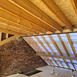 Usługi budowlane - Konstrukcja drewniana poddasza z ceglaną ścianą w Jeleśni. Widoczne elementy więźby dachowej i ocieplenia. Prace wykończeniowe w trakcie realizacji.