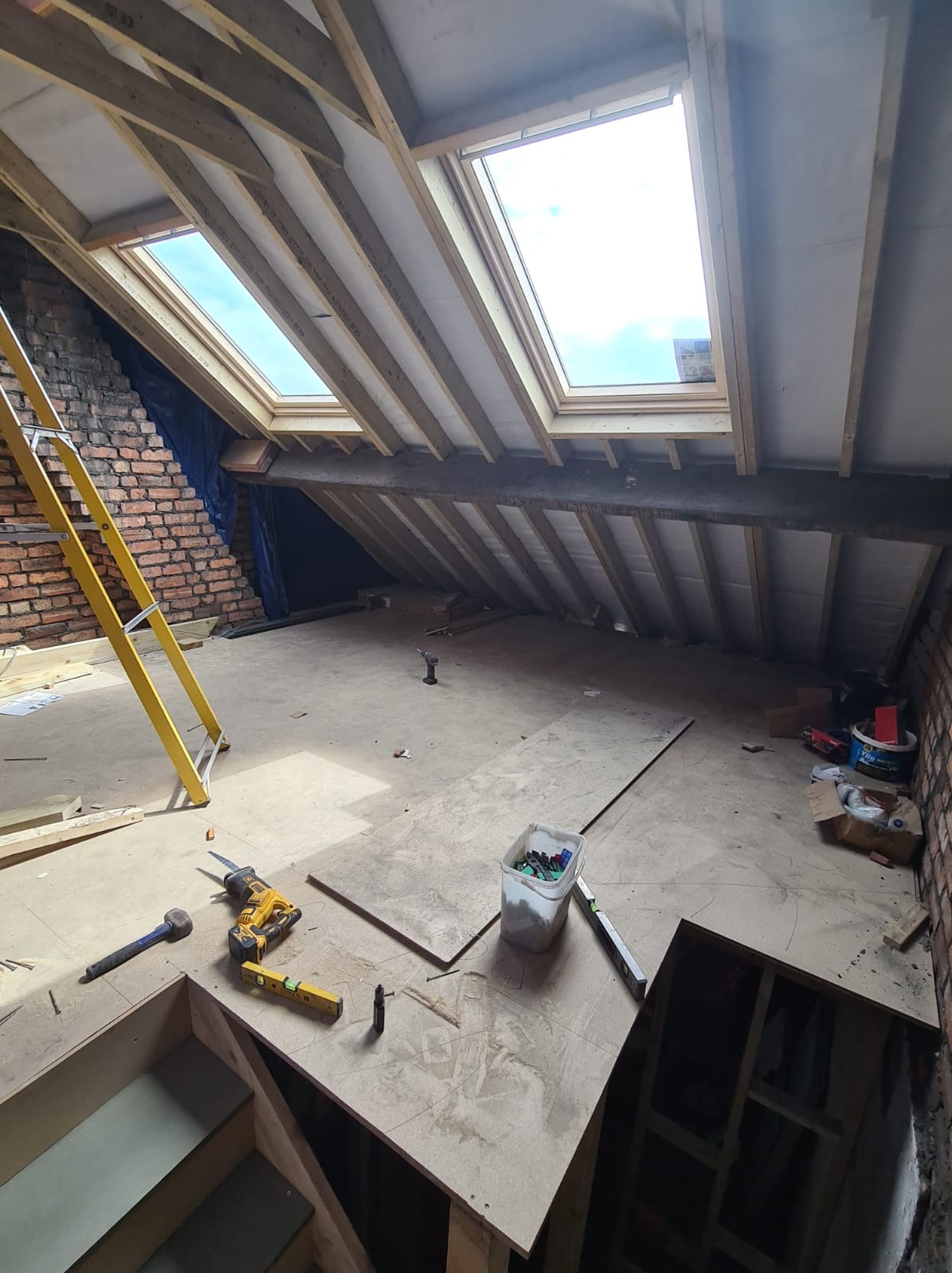 Adaptacja poddasza w Jeleśni: widok na konstrukcję dachu z oknami połaciowymi, narzędzia pracy i fragment podłogi w trakcie prac wykończeniowych. Widoczna drabina.