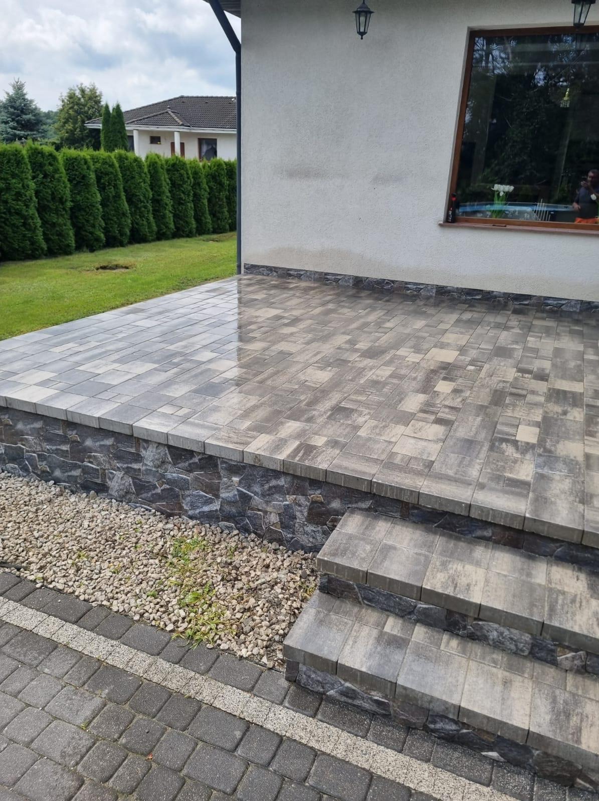 Wykończony taras z kostki brukowej w Bydgoszczy, z kamienną podmurówką i schodami. Widoczne detale ułożenia kostki i aranżacja z drobnym kamieniem.