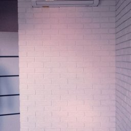 Eliz-Klima Wiktoria Leśko - Biały klimatyzator na ścianie z białej cegły w pokoju z szarą podłogą. Widoczny kabel zasilający. Minimalistyczny design.