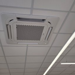 COLD-RES Dominik Markowski - Kasetonowa klimatyzacja Hisense zamontowana w suficie podwieszanym, widok z dołu, oświetlenie liniowe LED w tle. Biała kolorystyka urządzenia i sufitu.
