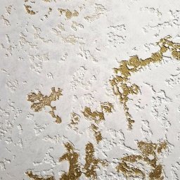 Artur Wojtysiak - Biała ściana z dekoracyjną, nieregularną fakturą i złotymi akcentami, tworzącymi unikalny wzór. Widoczne nierówności i detale wykończenia.