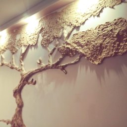 Artur Wojtysiak - Dekoracyjna płaskorzeźba drzewa z fakturą kory na ścianie, oświetlona od góry, tworząca unikalny element wystroju wnętrza.