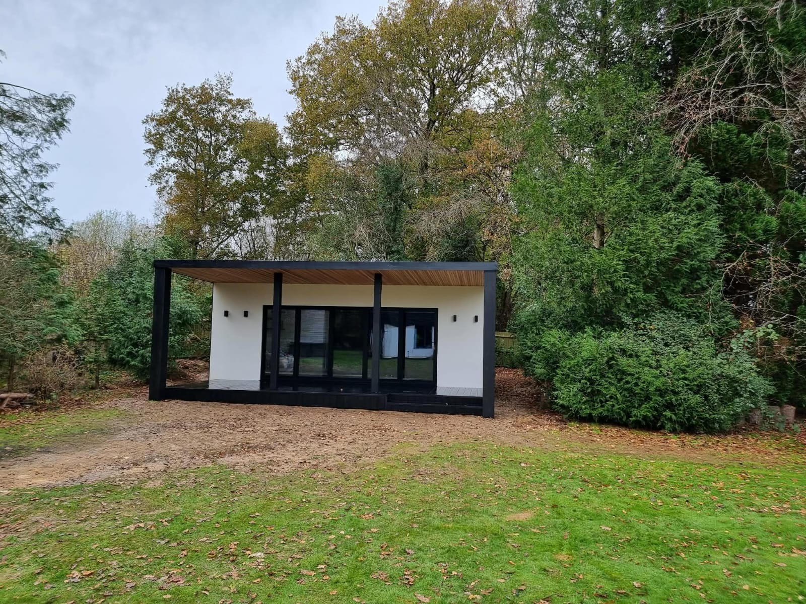 Nowoczesny, parterowy dom modułowy z płaskim dachem i dużymi przeszkleniami, otoczony zielenią. Minimalistyczna bryła wkomponowana w naturalne otoczenie.