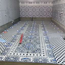 Sebastian Deruś - Układanie wzorzystych płytek w łazience, widoczne poziomica i klipsy dystansowe. Na ścianach również płytki z motywami. Etap prac wykończeniowych.