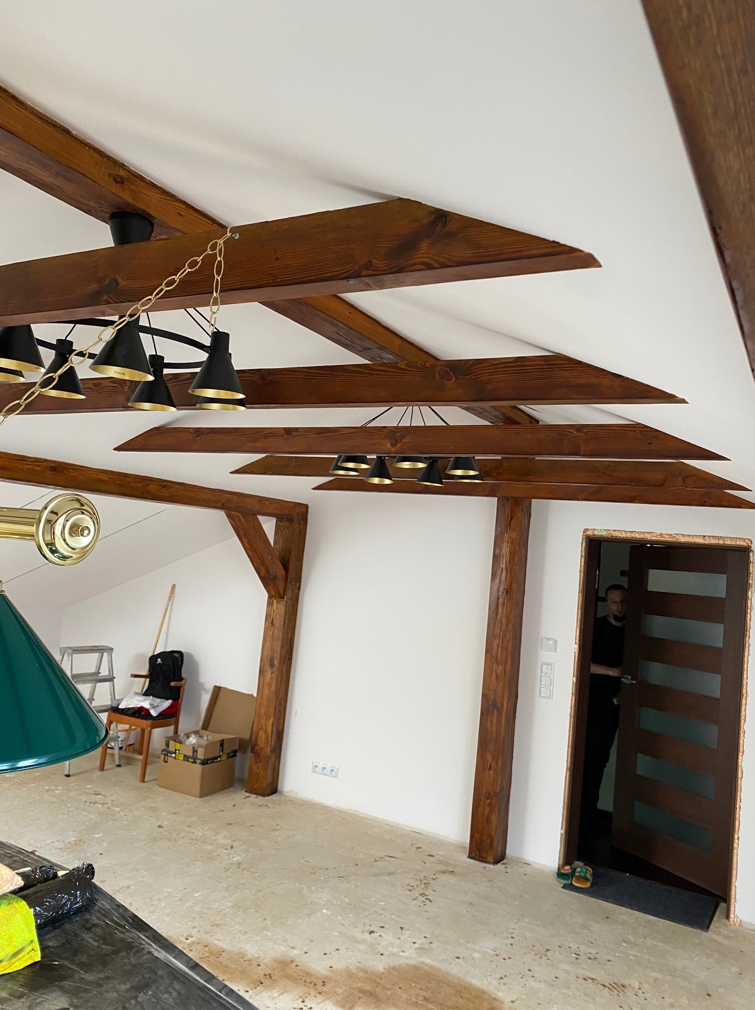 Strop z drewnianymi belkami i nowoczesnym oświetleniem w remontowanym wnętrzu. Widoczne przygotowania do dalszych prac wykończeniowych i montaż drzwi.