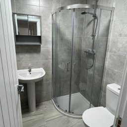 NRBT Ekspert - Mariusz Jakubas - Nowoczesna łazienka po remoncie: szare płytki, kabina prysznicowa narożna, umywalka na postumencie i toaleta. Minimalistyczny styl, czyste linie, świeżo po renowacji.