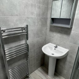 NRBT Ekspert - Mariusz Jakubas - Wyremontowana łazienka w szarościach: umywalka na postumencie, grzejnik drabinkowy i szafka z lustrem. Minimalistyczny design, płytki imitujące kamień.