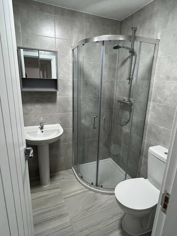 Nowoczesna łazienka po remoncie: szare płytki, kabina prysznicowa narożna, umywalka na postumencie i toaleta. Minimalistyczny styl, czyste linie, świeżo po renowacji.