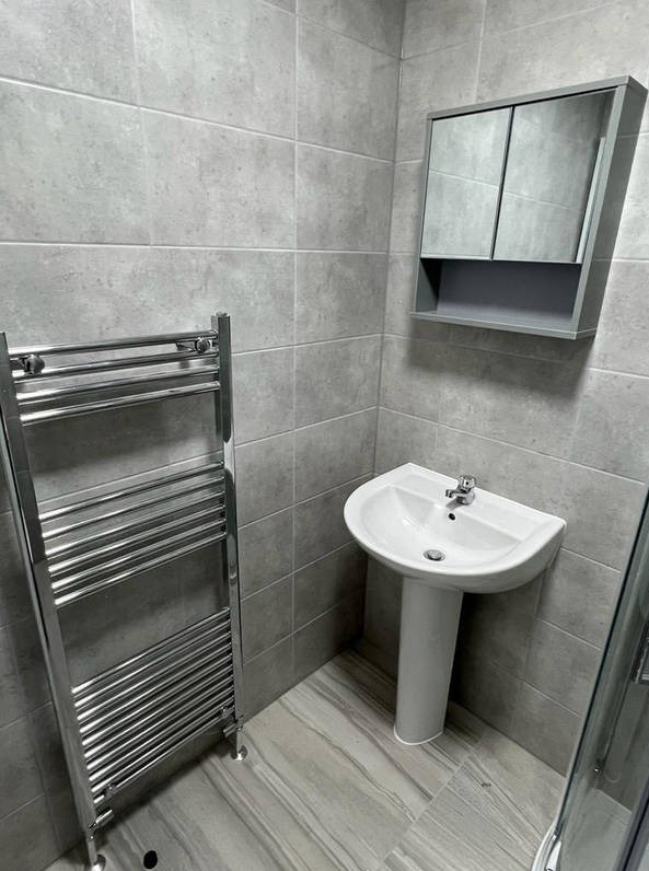 Wyremontowana łazienka w szarościach: umywalka na postumencie, grzejnik drabinkowy i szafka z lustrem. Minimalistyczny design, płytki imitujące kamień.