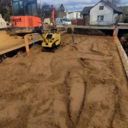 Firma budowlana Matbud - Wykonane wykopy pod fundamenty z użyciem pomarańczowej koparki Bobcat i żółtej zagęszczarki. Widoczne szalunki i przygotowany teren pod budowę domu.