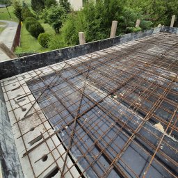 Firma budowlana Matbud - Zbrojenie stropu z betonu komórkowego, widok z góry. Siatka z prętów stalowych ułożona na czarnej folii, obrzeża z szarego betonu komórkowego. Prace budowlane w toku.