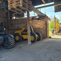 Firma budowlana Matbud - Wnętrze remontowanego budynku z maszynami budowlanymi: podnośniki teleskopowe i koparka. Widoczni pracownicy. Elementy konstrukcyjne w trakcie montażu.