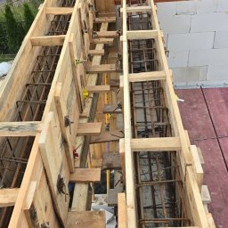 Firma budowlana Matbud - Szczegółowe ujęcie szalunku zbrojeniowego na budowie domu, widoczne elementy drewniane i stalowe pręty zbrojeniowe, z perspektywy góry, w tle ściany z białego bloczka.