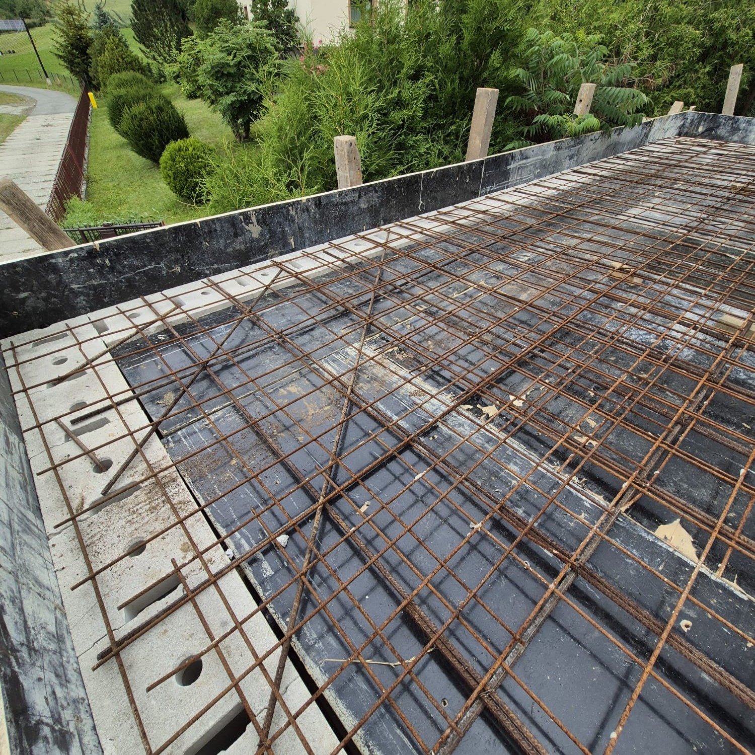 Zbrojenie stropu z betonu komórkowego, widok z góry. Siatka z prętów stalowych ułożona na czarnej folii, obrzeża z szarego betonu komórkowego. Prace budowlane w toku.
