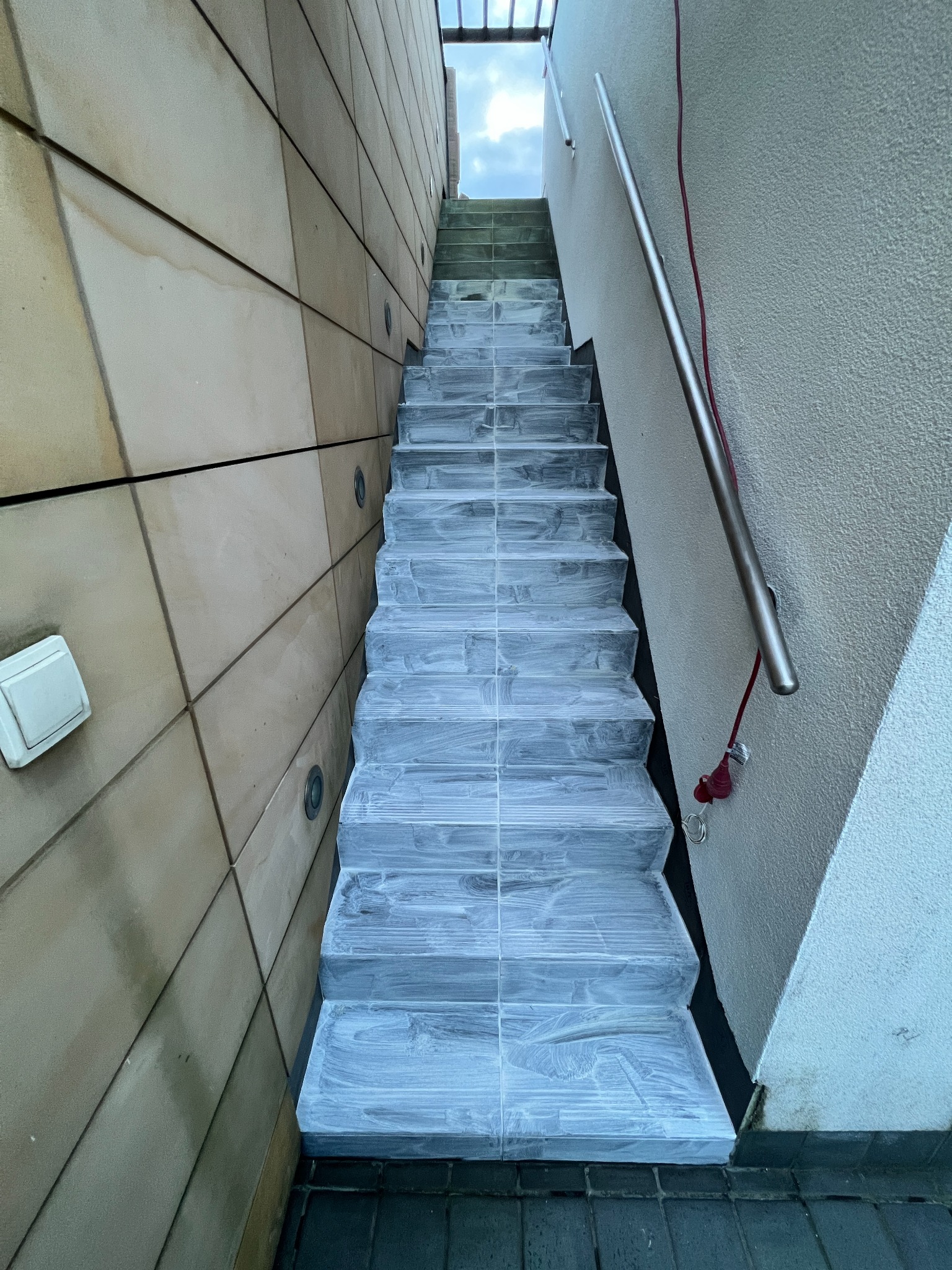 Schody zewnętrzne po czyszczeniu w Wojcieszycach. Widoczne płytki pokryte środkiem czyszczącym, metalowa barierka i fragment elewacji budynku.