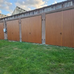 SpecStal Dawid Kędzierski - Brązowe bramy garażowe z pionowymi panelami, zamontowane w rzędzie w budynku z panelami słonecznymi na dachu. Na pierwszym planie narzędzia na trawie.