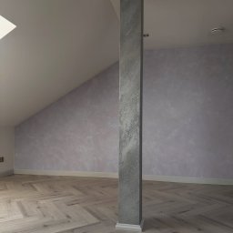 ZUBRA SPÓŁKA Z OGRANICZONĄ ODPOWIEDZIALNOŚCIĄ - Pokój na poddaszu po malowaniu ścian z efektem dekoracyjnym, drewniana podłoga w jodełkę, kolumna w szarym kolorze. Widok na skośny sufit i okno dachowe.
