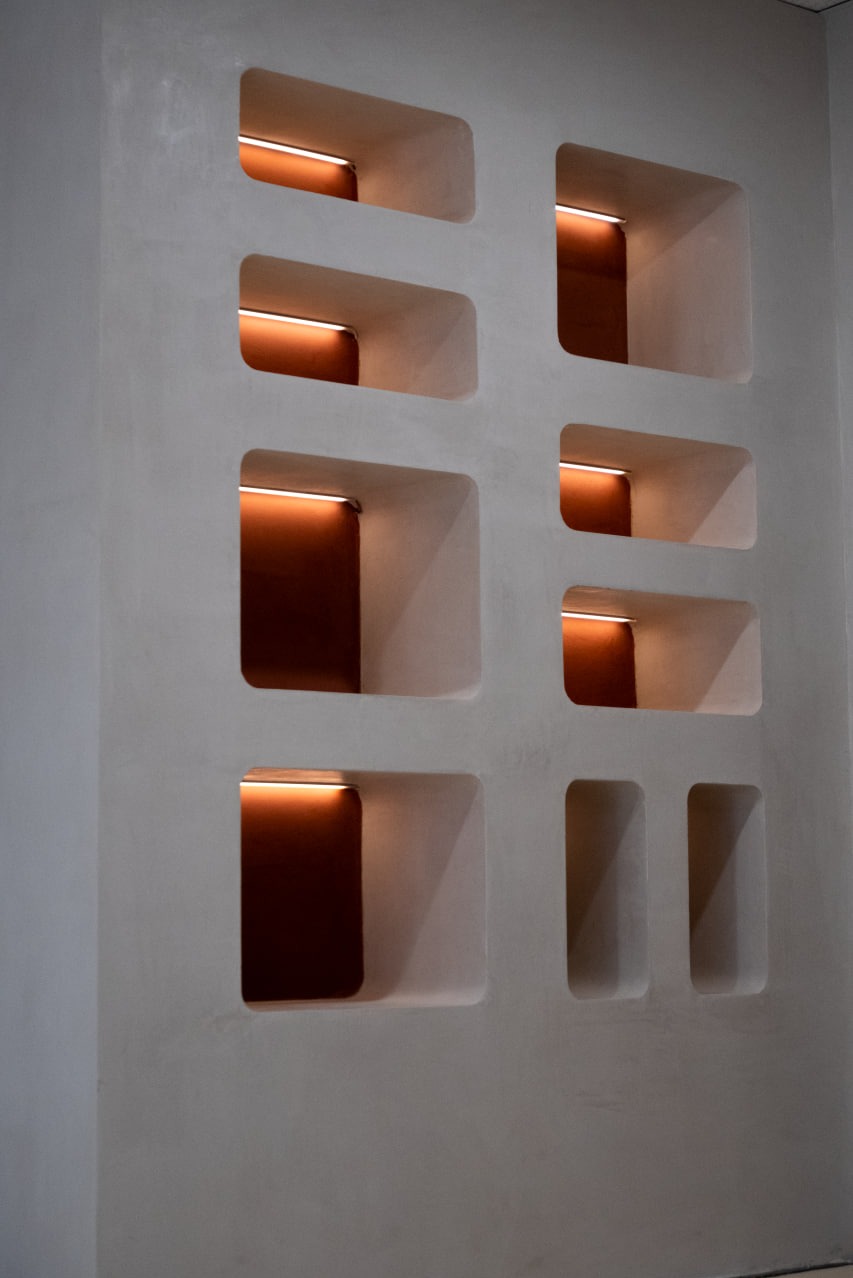 Ściana z wnękami oświetlonymi ciepłym światłem LED, wykończona gładzią w odcieniach bieli i szarości. Minimalistyczny design, nowoczesne wykończenie wnętrza.