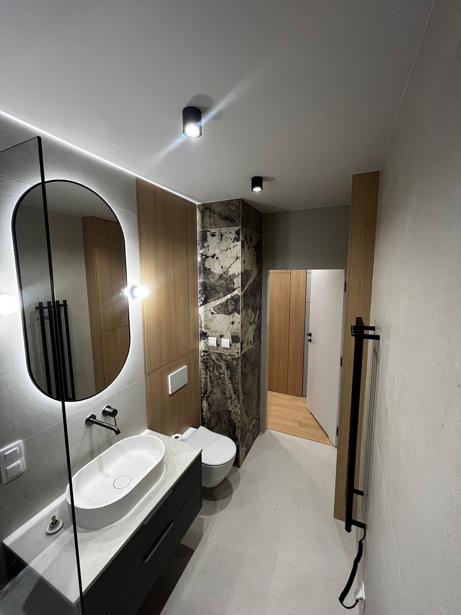 Nowoczesna łazienka po remoncie: owalne lustro z podświetleniem LED, umywalka nablatowa, marmurowe akcenty i drewniane panele. Minimalistyczny design.
