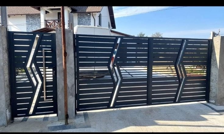 Nowoczesna, czarna brama wjazdowa z poziomymi szczeblami i geometrycznym wzorem, osadzona na betonowych słupkach, na tle domu z białym busem.