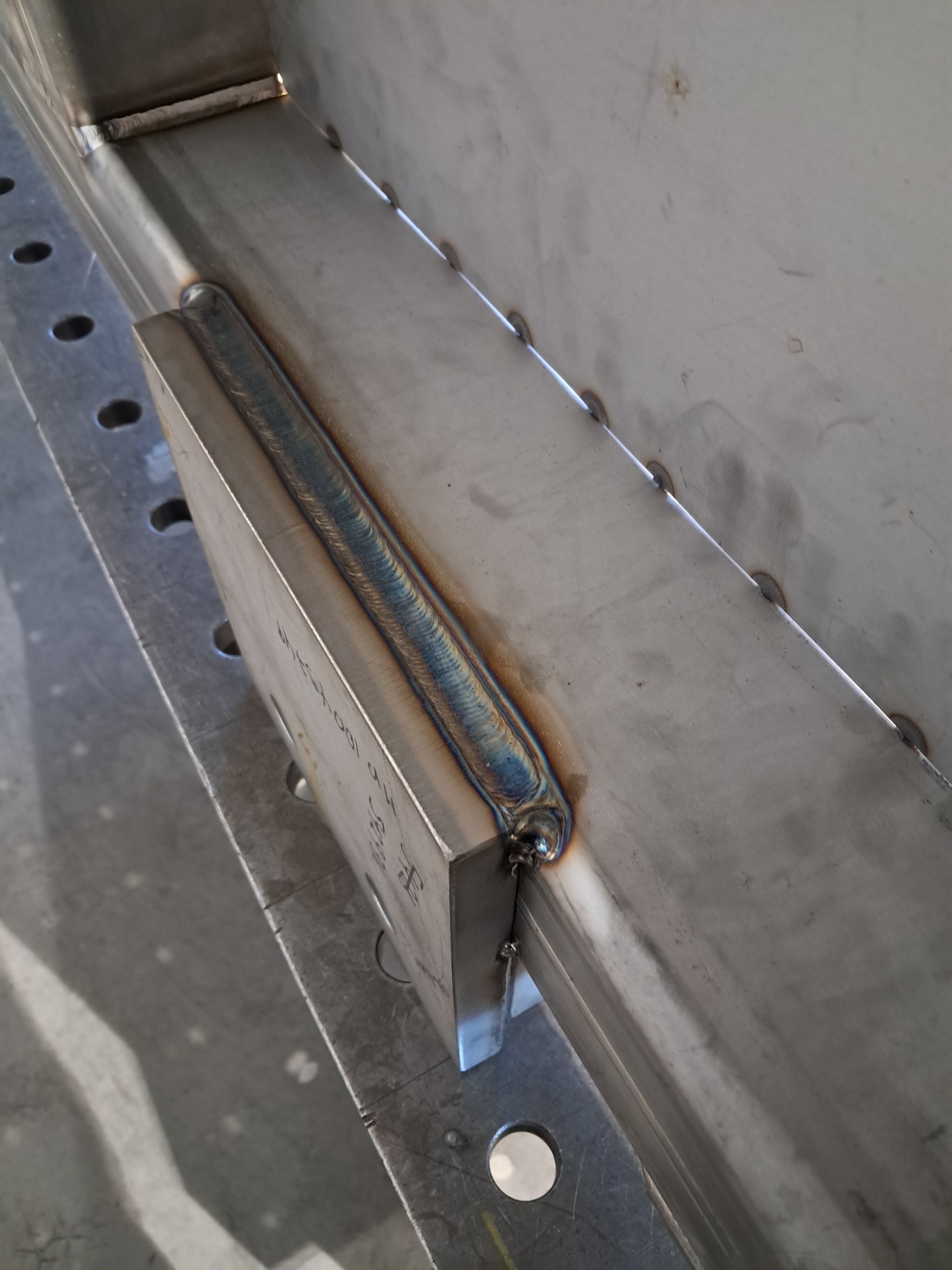 Precyzyjne spawy na metalowej konstrukcji, widoczne charakterystyczne przebarwienia termiczne, świadczące o wysokiej jakości wykonania. Detal z bliska.