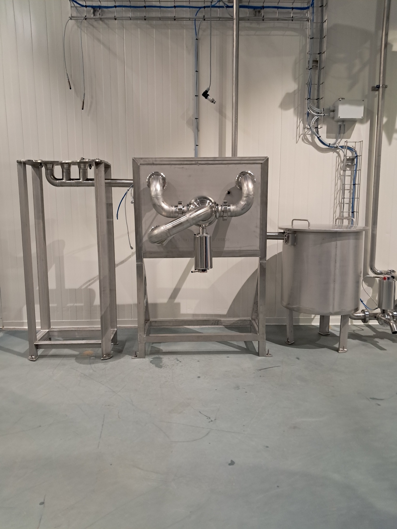 Kompleksowa instalacja ze stali nierdzewnej w sterylnym pomieszczeniu, z widocznymi rurami, zbiornikiem i ramami nośnymi. Elementy połączone spawami.