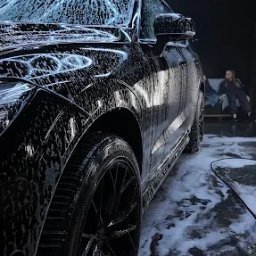 NZK AUTO DETAILING - Olszewnica Stara - Czarny SUV pokryty pianą w myjni, widok z boku, oświetlenie LED w kształcie plastra miodu, osoba w tle. Detailing felg i karoserii.