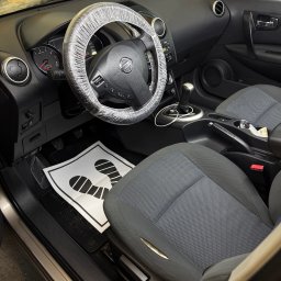 NZK AUTO DETAILING - Olszewnica Stara - Wnętrze samochodu Nissan Qashqai z założonym pokrowcem ochronnym na kierownicy i matą pod nogi, przygotowane do czyszczenia tapicerki.