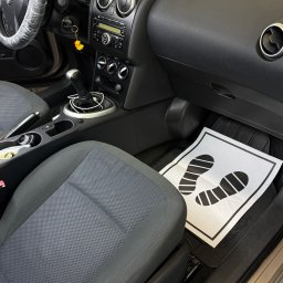 NZK AUTO DETAILING - Olszewnica Stara - Wnętrze auta po praniu tapicerki w Olszewnicy Starej. Czyste siedzenia, deska rozdzielcza i dywaniki z symbolem stóp. Kierownica w folii ochronnej.