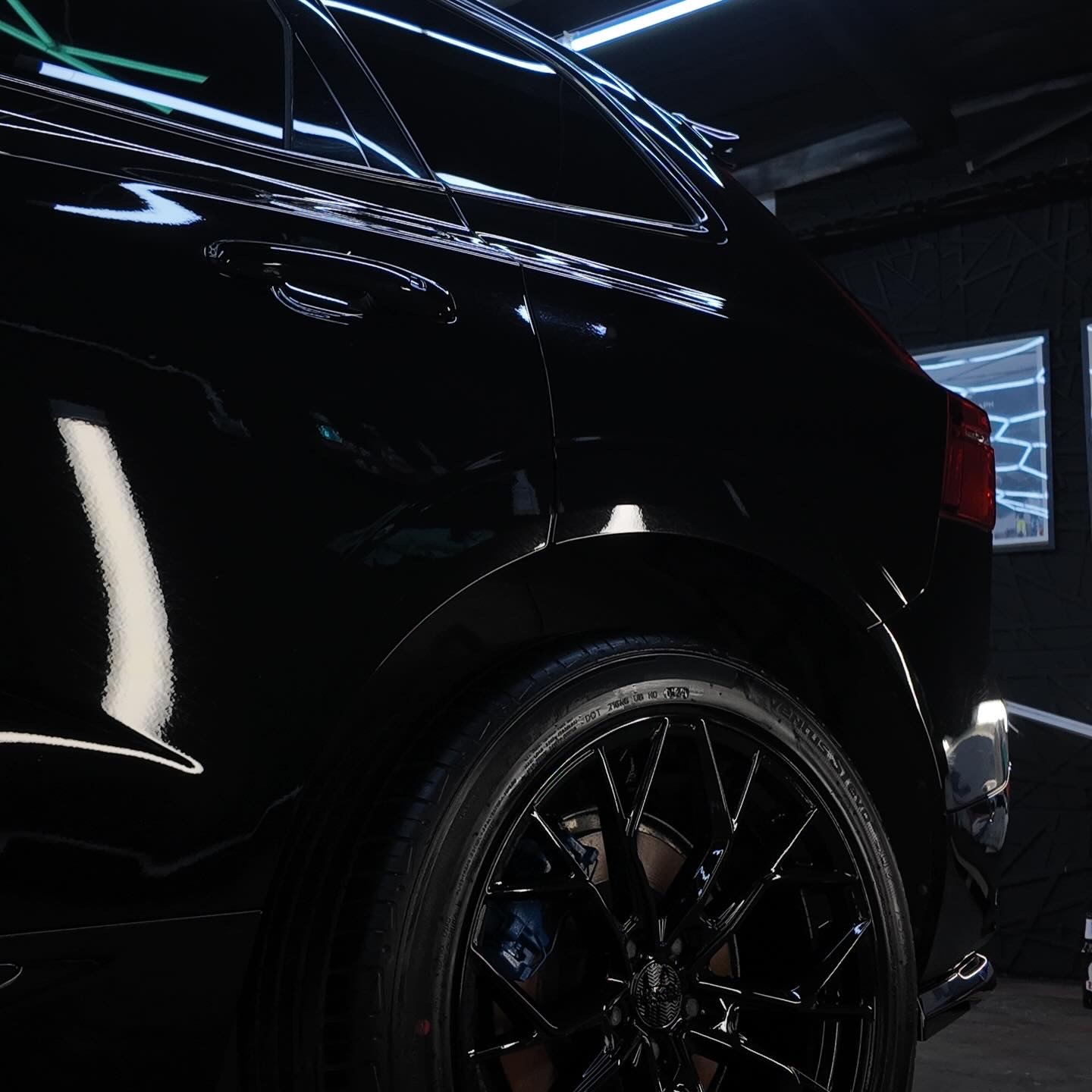 Błyszczący, czarny SUV po detailingu. Widoczne odbicia światła na lakierze i felgi z niebieskimi zaciskami hamulcowymi. Perfekcyjny połysk.