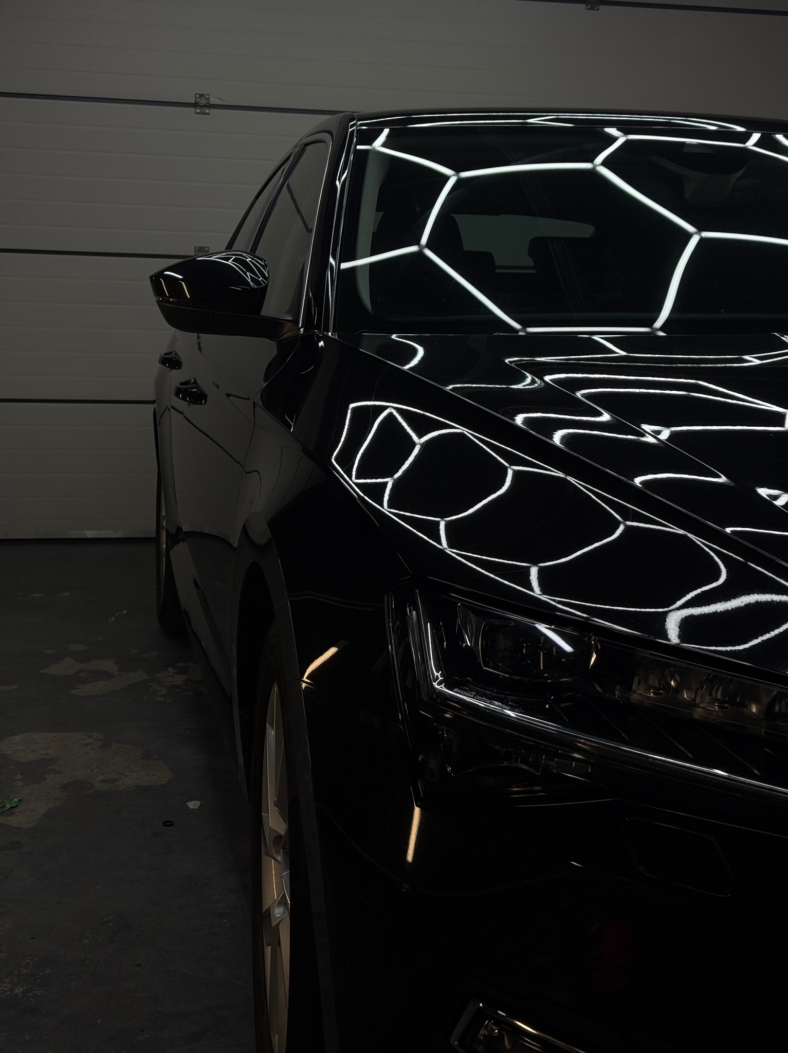 Błyszczący, czarny samochód Skoda Superb po myciu, z widocznymi refleksami światła na karoserii. Ujęcie z bliska, ukazujące detale lampy i maski.