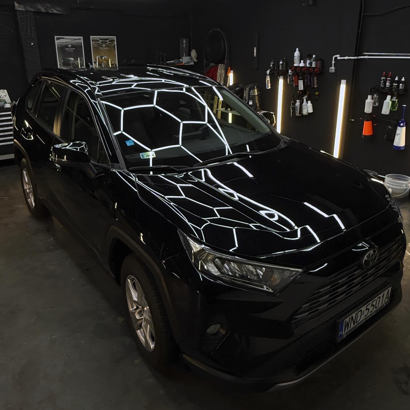 Błyszczący, czarny SUV Toyota RAV4 po detailingu, z widocznym odbiciem lamp w lakierze, w profesjonalnym studiu z czarnym tłem i narzędziami do pielęgnacji.