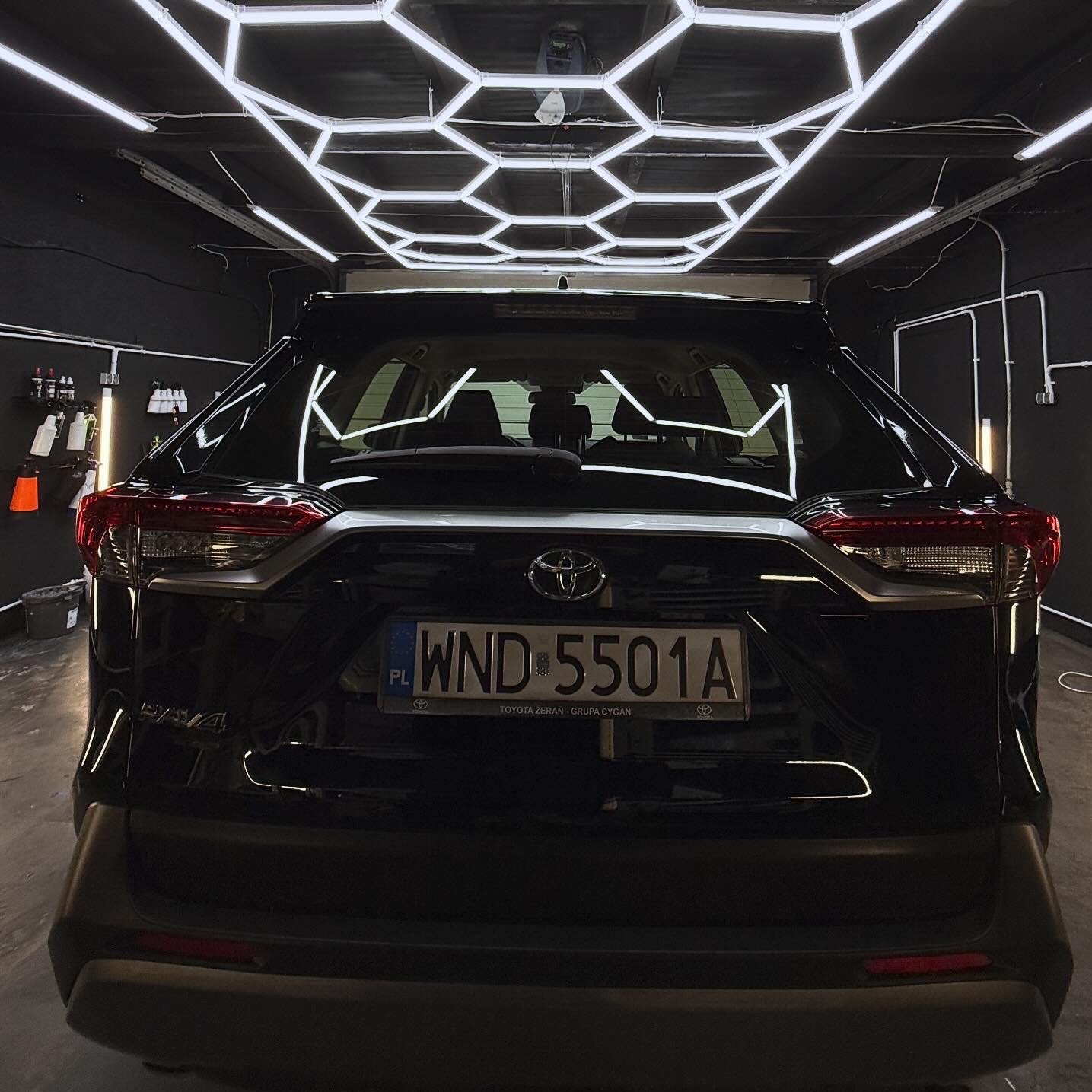 Błyszczący, czarny SUV Toyota RAV4 po myciu, widziany z tyłu w dobrze oświetlonym garażu z heksagonalnym oświetleniem sufitowym. Tablica rejestracyjna WND 5501A.