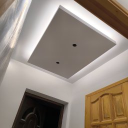 Łukasz Książek - Podwieszany sufit z oświetleniem LED w kształcie kwadratu, widok z dołu, z fragmentami drzwi po bokach. Dwa otwory na oświetlenie punktowe.