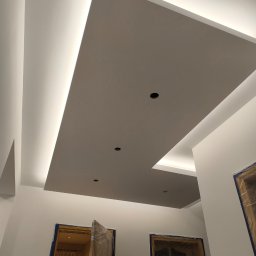 Łukasz Książek - Podwieszany sufit z oświetleniem LED w nowocześnie wykończonym wnętrzu. Widoczne otwory na oświetlenie punktowe i zabezpieczone folią drzwi.