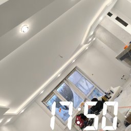 Łukasz Książek - Białe wnętrze po remoncie z oknem, widoczne wykończone ściany, sufit z oświetleniem punktowym i częściowo zakryte podłogi. W tle okno z widokiem na drzewa.