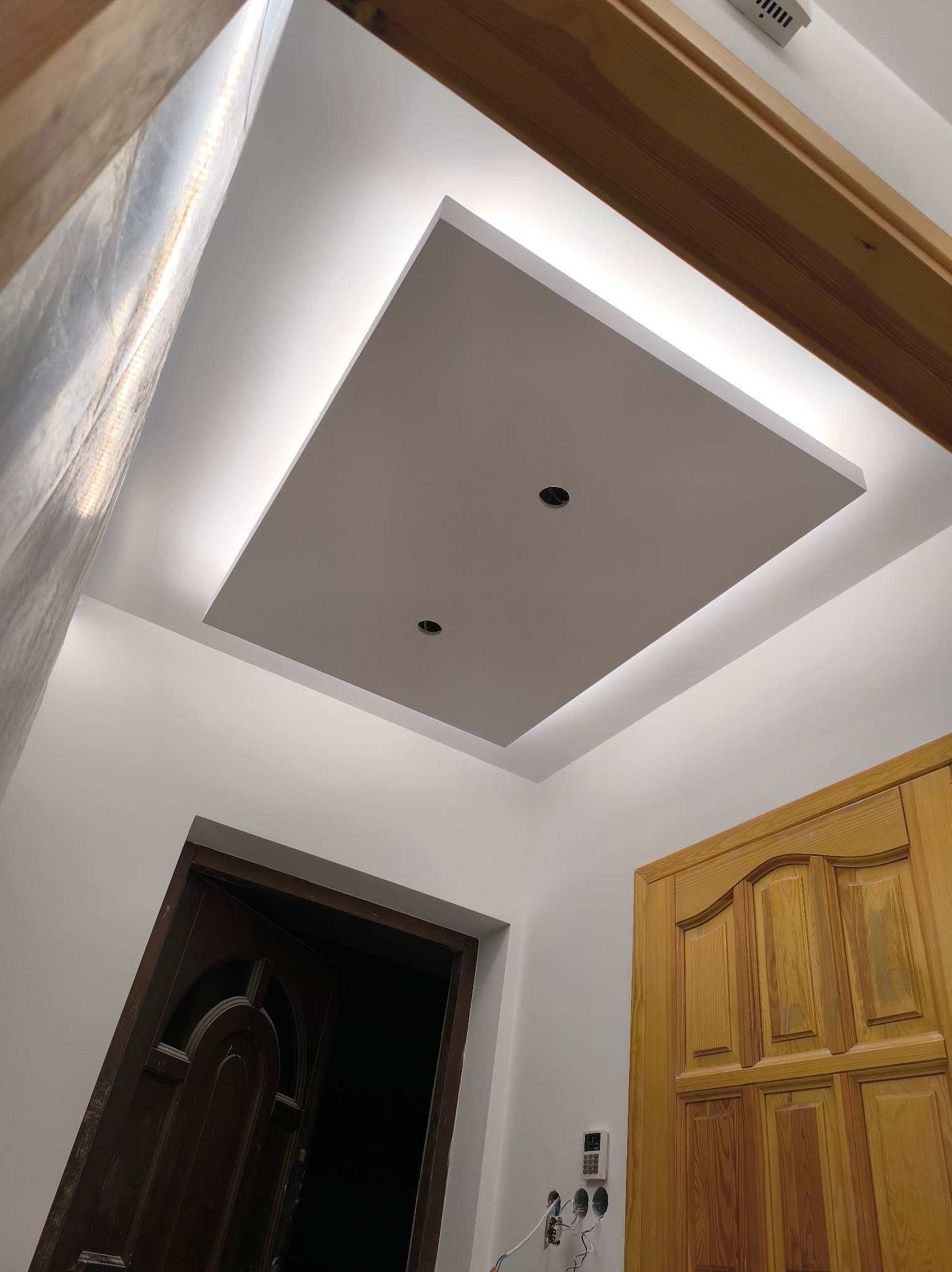 Podwieszany sufit z oświetleniem LED w kształcie kwadratu, widok z dołu, z fragmentami drzwi po bokach. Dwa otwory na oświetlenie punktowe.