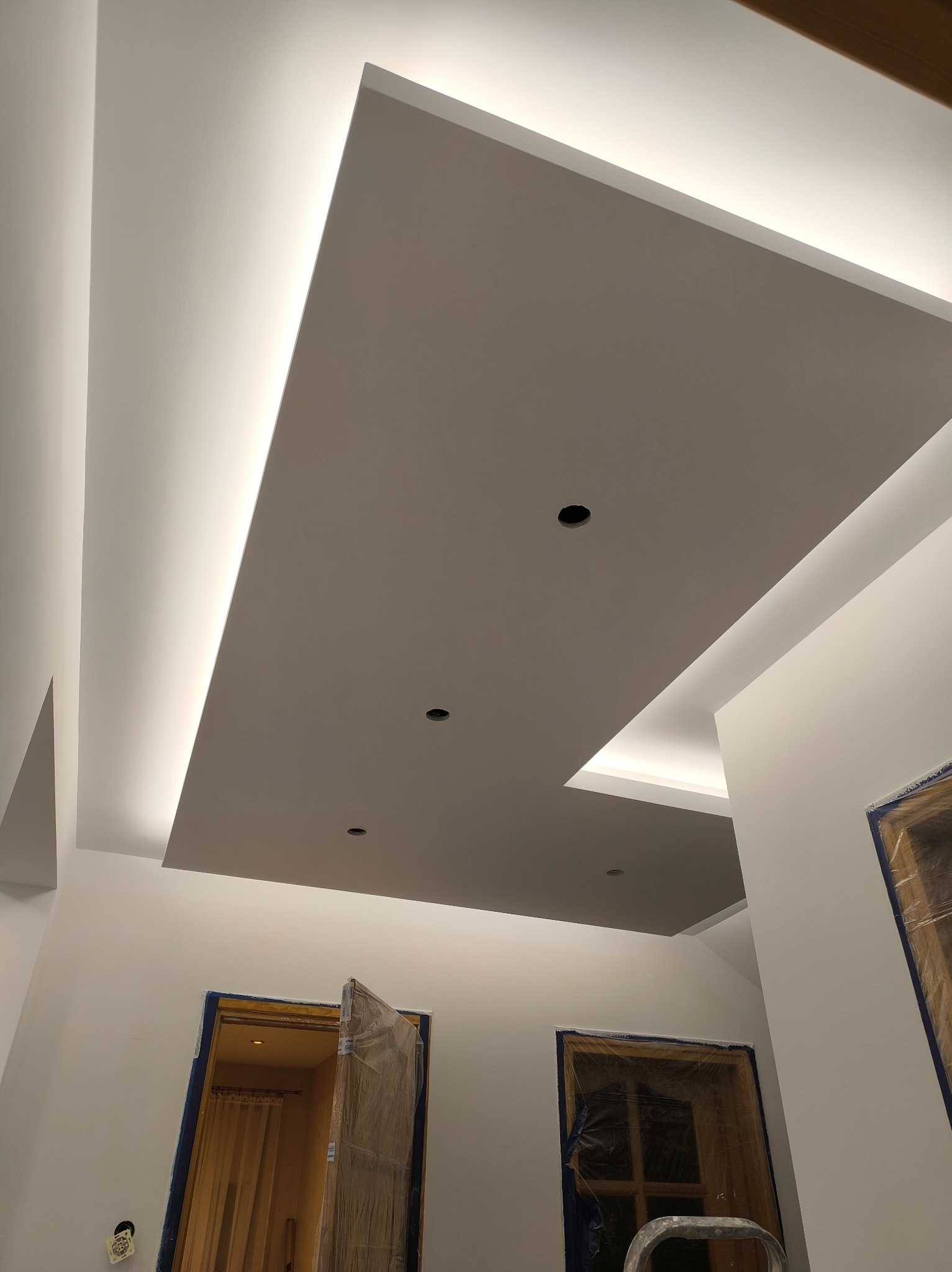 Podwieszany sufit z oświetleniem LED w nowocześnie wykończonym wnętrzu. Widoczne otwory na oświetlenie punktowe i zabezpieczone folią drzwi.