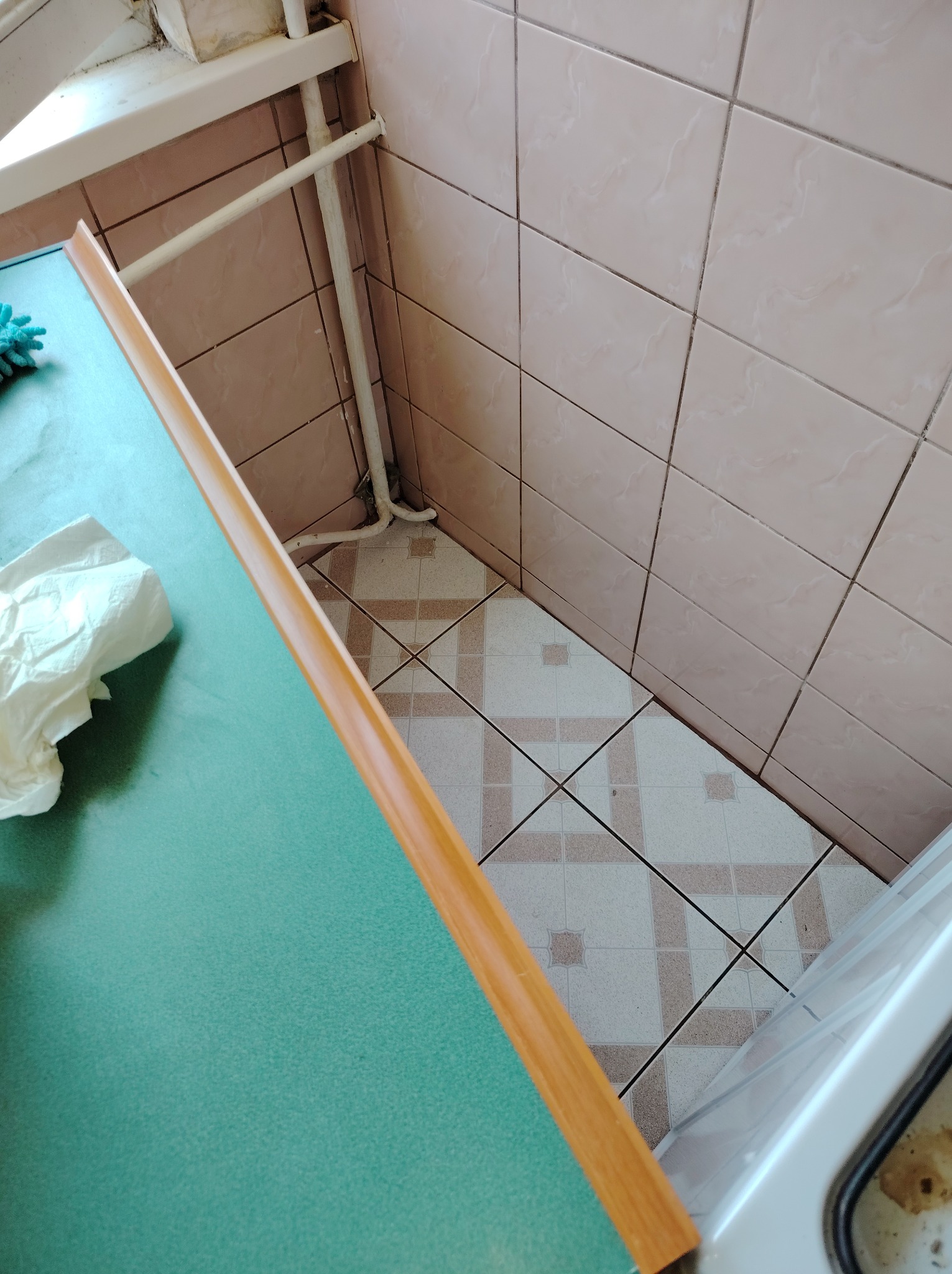 Fragment kuchni po czyszczeniu: zielony blat z ściereczką, płytki na ścianie i podłodze. Widoczne rury i okno. Ujęcie z góry, podkreślające detale.