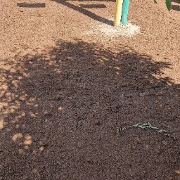 FHU Mateusz Adamiec - Przygotowany teren pod siew trawy, widoczny siewnik w tle, obok drzewo z zielonymi liśćmi. Ziemia ma ciemnobrązowy kolor.