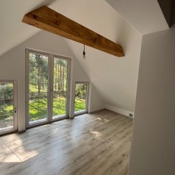 BarTix-Art - Jasne poddasze z drewnianą belką stropową i trzema oknami z widokiem na las. Parkiet w odcieniach szarości. Ściany pomalowane na biało. Minimalistyczny design.