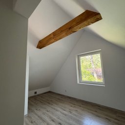 BarTix-Art - Poddasze po remoncie: drewniana belka, okno z widokiem na zieleń, panele podłogowe imitujące drewno, świeżo pomalowane ściany na biało. Minimalistyczny styl.