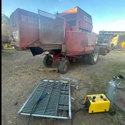 Paweł Kulaszewicz - Spawanie metalowej kraty na tle kombajnu rolniczego. Widoczny spawacz, butla z gazem i spawarka inwertorowa. Praca w toku, na zewnątrz.