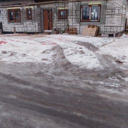 KUKIS INSTALL SZYMON KUKIEŁKA - Surowy stan domu w budowie z częściowo położonym dachem z dachówki, widoczne okna i drzwi, teren wokół pokryty śniegiem. Ujęcie z dołu.